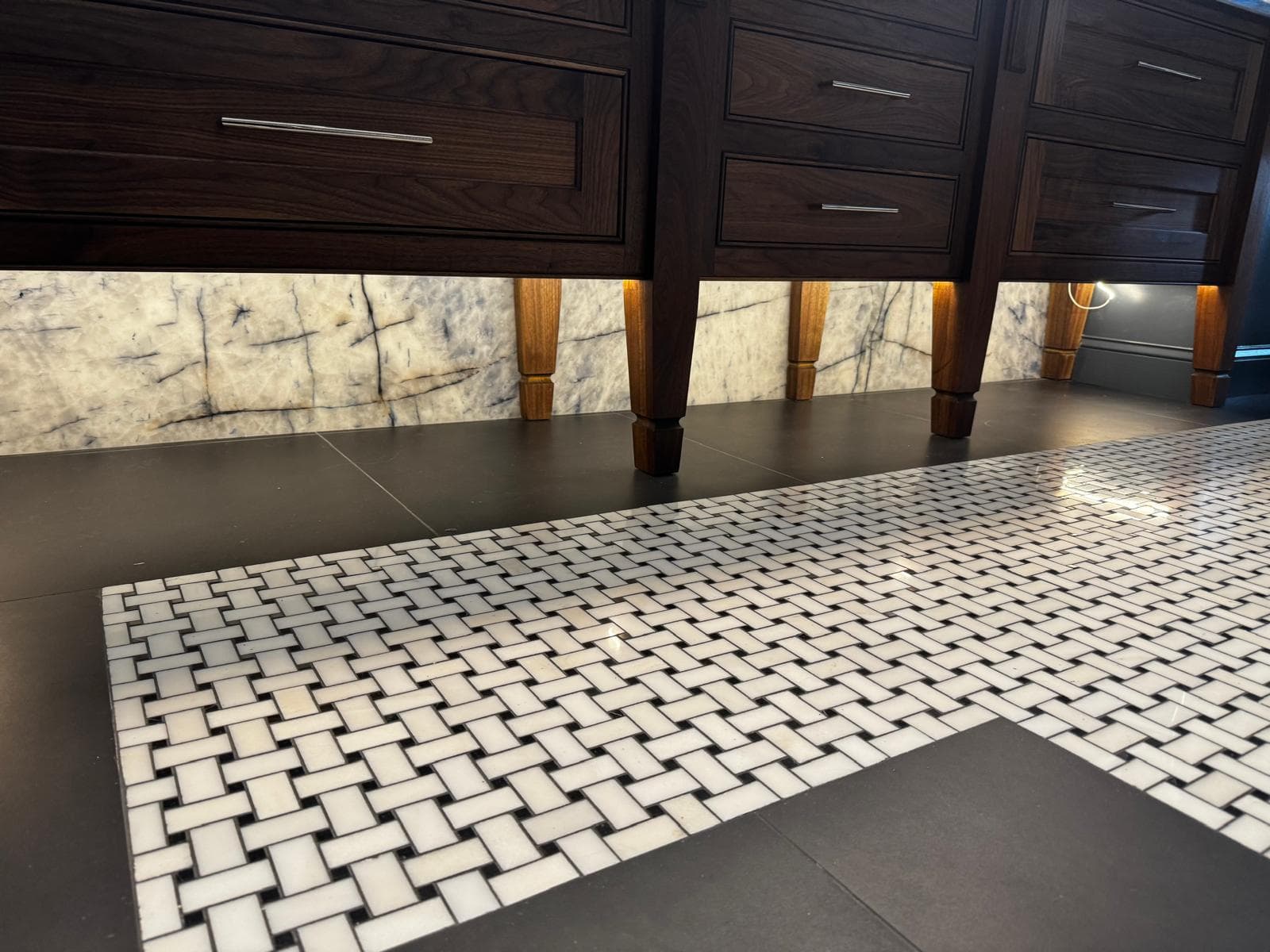 Basketweave marble mosaic floor tile beside walnut vanity legs, Atlanta, GA